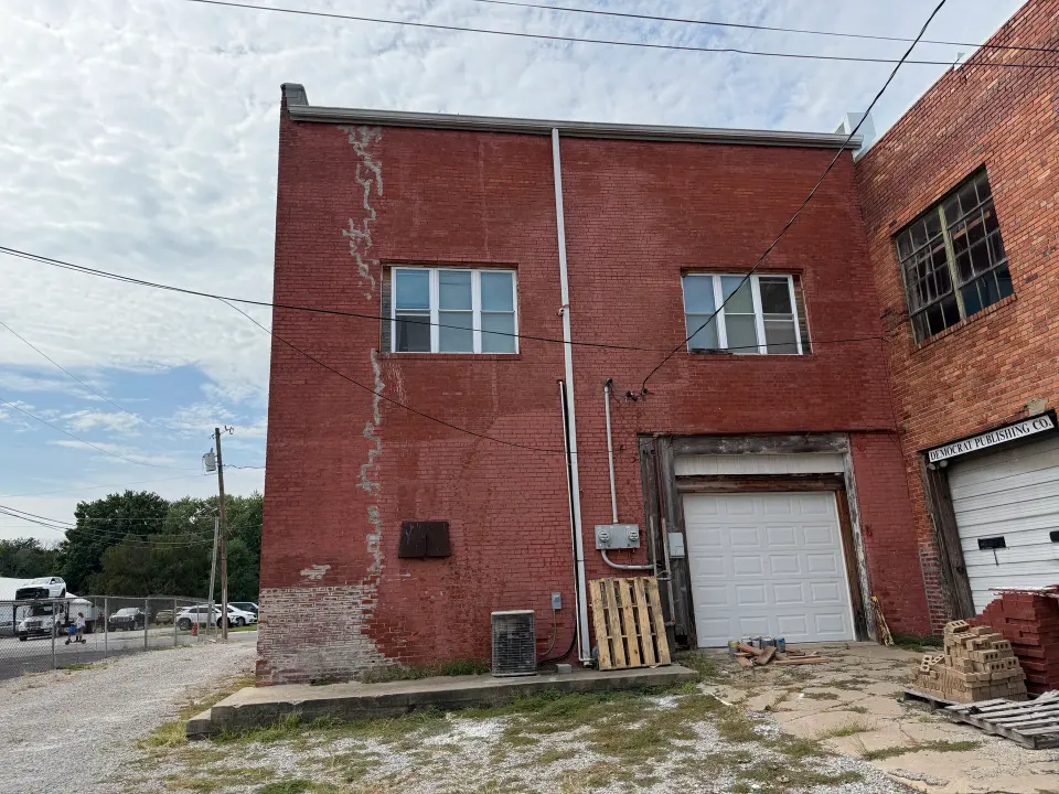 Rear of Old City Hall with upper windows, a ground-floor garage door and existing utility equipment.