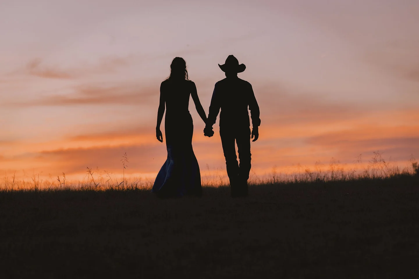 Silhouettes of Ben and Clarissa holding hands against an orange and pink country sunset.